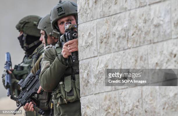 An Israeli soldier aims his rifle from behind a wall during a military operation after the Israeli army forces killed Palestinian gunmen, near Elon...