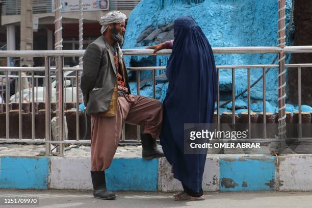 An Afghan man talks to a burqa-clad woman as they stand along a street in Fayzabad district of Badakhshan province on April 11, 2023.