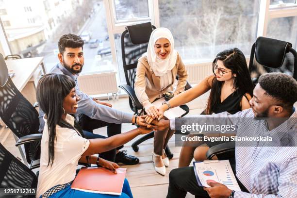 ethnic business people holding their arms together in the office. - office small business stock-fotos und bilder