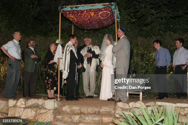 An Orthodox Jewish wedding, the couple stands under the Chuppah or canopy and the Rabbi talks to them, the bridegroom wears a talith and the bride...