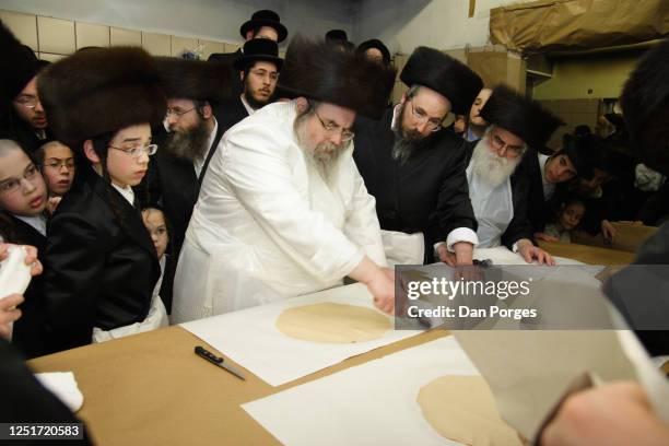 Rabbi Yissachar Dov Rokeach, leader of the Belz Hassidic community uses a tool with rolling pins to pin holes in a flattened piece of dough to put in...