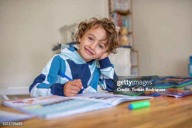 portrait of smiling little boy doing homework at table at home - boy curly blonde stock pictures, royalty-free photos & images