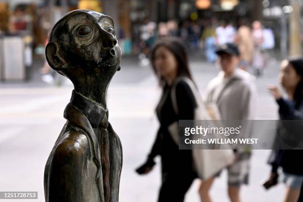 People walk past a statue of a businessman in Melbourne on April 12, 2023. - Statues of three businessmen by artist Alison Weaver were a gift from...