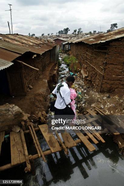 Woman and her child cross a bridge over a filthy drainage channel in the Kibera slum in Nairobi, Kenya, 10 December 2003. With nearly half a million...