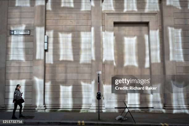 Young woman walks beneath reflected light on the high walls of the Bank of England in Batholomew Lane EC2, in the City of London, aka the Square Mile...