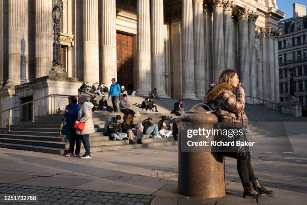 Young woman smokes a cigarette beneath the front facade of St Paul's Cathedral in the City of London, aka the Square Mile - the capital's financial...