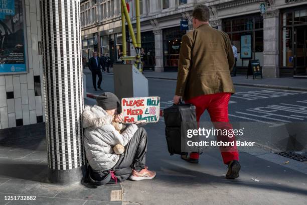 Man wearing red trousers strides past a street beggar near Liverpool Street Station in the City of London, aka the Square Mile - the capital's...