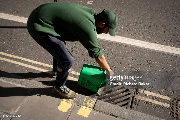 City cleaner pours dirty water down the drain in the City of London, aka the Square Mile - the capital's financial district, on 4th April 2023, in...