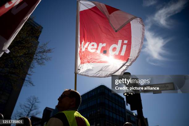 April 2023, Berlin: A participant of a rally on the occasion of the warning strike at Galeria, Ikea and Thalia holds a Verdi flag in front of the...