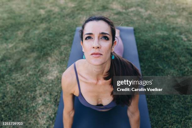 high angle front view of a middle aged woman 35-39 years old doing a snake yoga pose in the grass - 35 39 years stockfoto's en -beelden