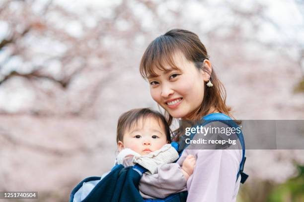 mother embracing her small baby in front of cherry blossom tree - portrait of a happy baby girl against cherry blossom tree stock pictures, royalty-free photos & images