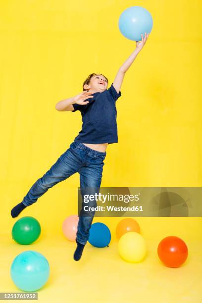 full length of boy catching balloon while playing against yellow background - child balloon studio photos et images de collection