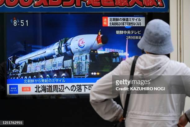 Woman watches street TV broadcasting breaking news of a North Korean missile launch in Tokyo on April 13, 2023. - Japanese Prime Minister Fumio...