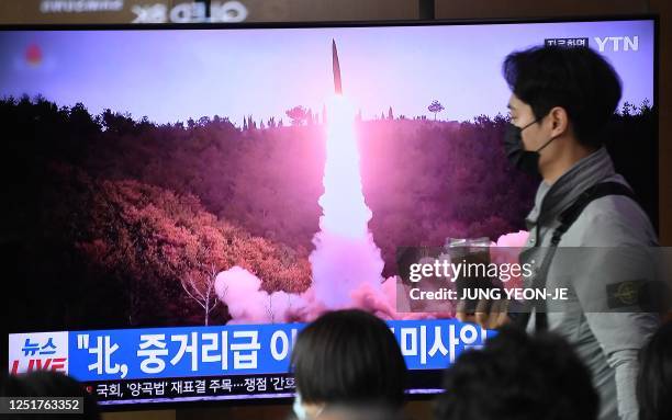 Man walks past a television screen showing a news broadcast with file footage of a North Korean missile test, at a railway station in Seoul on April...