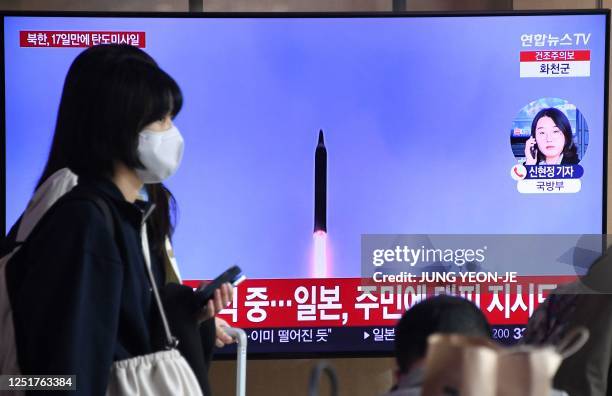 Woman walks past a television screen showing a news broadcast with file footage of a North Korean missile test, at a railway station in Seoul on...