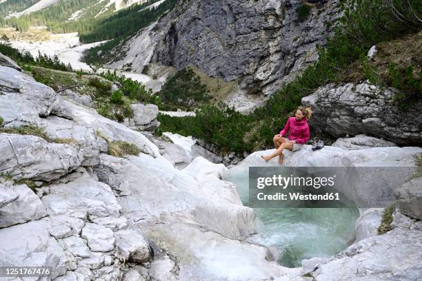 female tourist enjoying while splashing water with leg in stream against mountain - gebirgsbach stock-fotos und bilder