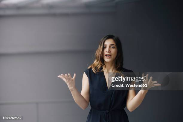 portrait of gesturing young businesswoman against grey background - speech stock pictures, royalty-free photos & images