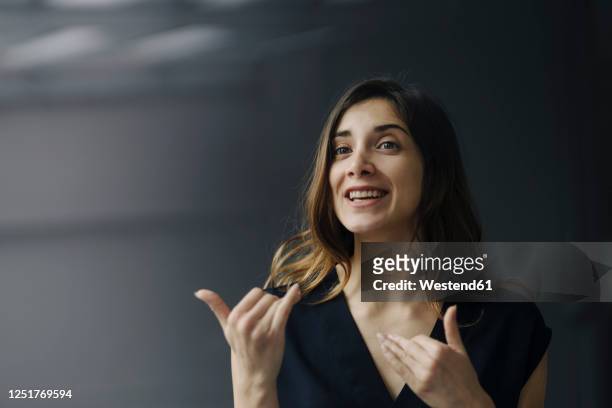 portrait of gesturing young businesswoman against grey background - spiegare foto e immagini stock