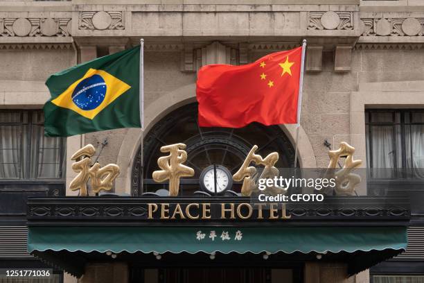 Chinese and Brazilian national flags flutter in the wind above the main entrance of the Peace Hotel on Nanjing Road Pedestrian street in Shanghai,...