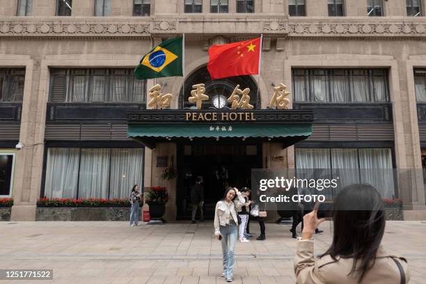 Chinese and Brazilian national flags flutter in the wind above the main entrance of the Peace Hotel on Nanjing Road Pedestrian street in Shanghai,...