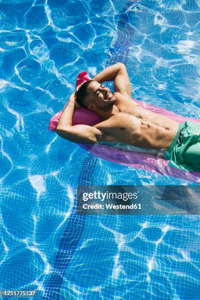 shirtless handsome young man with hands behind head relaxing on airbed in swimming pool - luftmatratze von oben stock-fotos und bilder