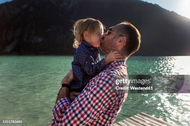 father and daughter kissing against mountain and lake at achensee, tyrol state, austria - beso en la boca fotografías e imágenes de stock