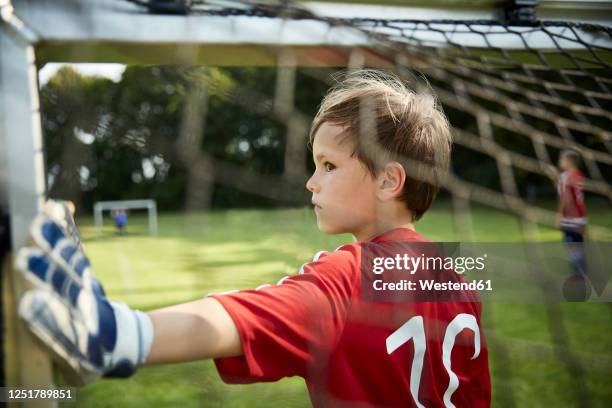 serious boy in soccer uniform holding goal post at field - goalkeeper gloves stock pictures, royalty-free photos & images