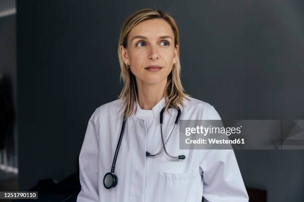portrait of doctor against grey background looking at distance - arzt portrait stock-fotos und bilder