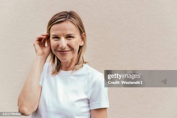 portrait of smiling blond woman wearing white t-shirt in front of light wall - woman smiling white background stock-fotos und bilder