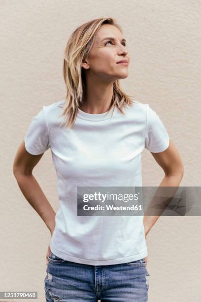 portrait of blond woman wearing white t-shirt in front of light wall looking up - aufschauen stock-fotos und bilder