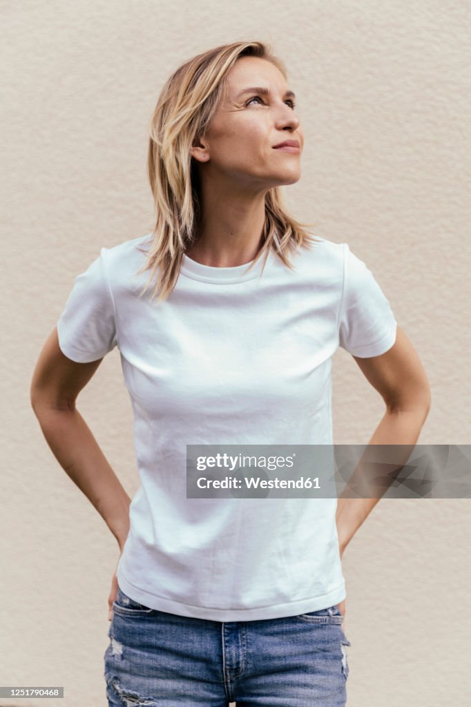 Portrait of blond woman wearing white t-shirt in front of light wall looking up
