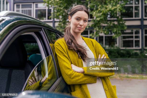 portrait of young woman with arms crossed leaning at her car - driver portrait stockfoto's en -beelden