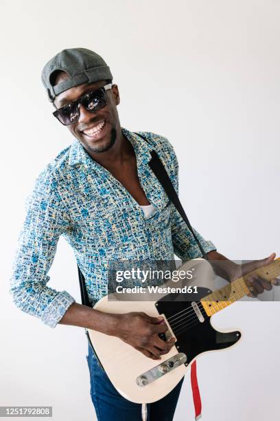 portrait of smiling young male pop musician playing guitar against white background - pop musician fotografías e imágenes de stock