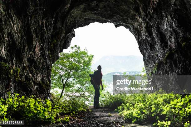 male explorer standing at cave entrance - cave entrance stock pictures, royalty-free photos & images