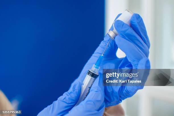 a young doctor in blue protective glove is holding a medical syringe and vial - covid 19 vaccine stock pictures, royalty-free photos & images