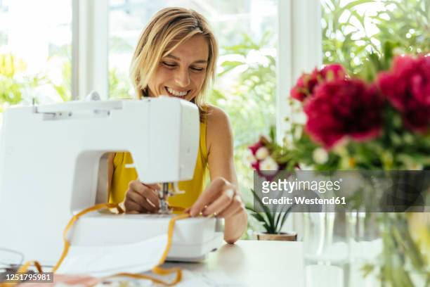 smiling woman sewing face masks at home - frau nähen stock-fotos und bilder