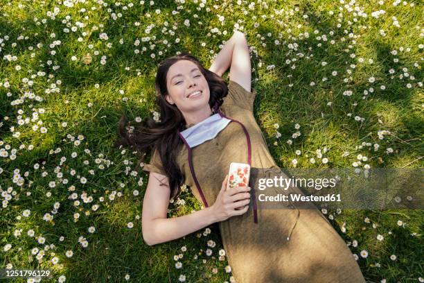 woman with let down face mask enjoying her free time while lying on grass with daisies - germany covid stock pictures, royalty-free photos & images