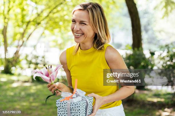happy woman in nature holding lily flower and gift - german birthday stock pictures, royalty-free photos & images