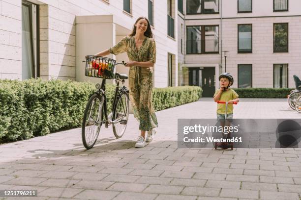 smiling mother with bicycle and son with scooter in the city - walking with bike stock-fotos und bilder