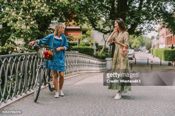 two women with bicycle and face mask walking on a bridge - chatting park stockfoto's en -beelden