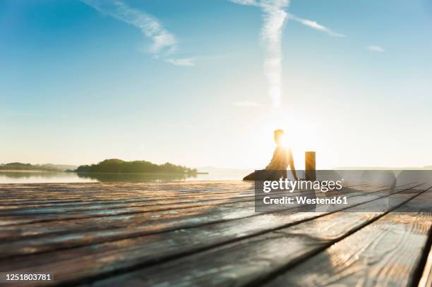 young man sitting on boardwalk at lake enjoying sunrise - boardwalk stockfoto's en -beelden