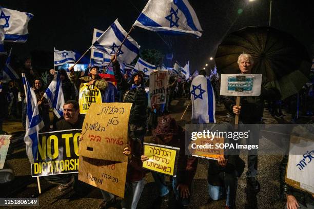 Anti reform protestors hold Israeli flags and placards that are a sarcastic response to Netanyahu's last speech about taking responsibility for...