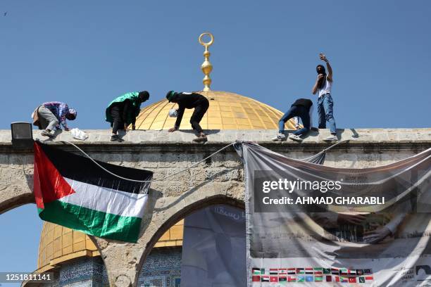 Youths hang a Palestinian national flag and a banner in front of the Dome of the Rock mosque, following the Friday noon prayers at the Al-Aqsa mosque...