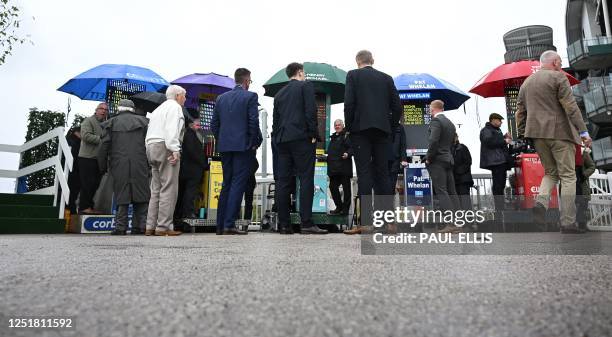 Racegoers look at the odds at bookmakers' betting stands on the second day of the Grand National Festival horse race meeting at Aintree Racecourse in...