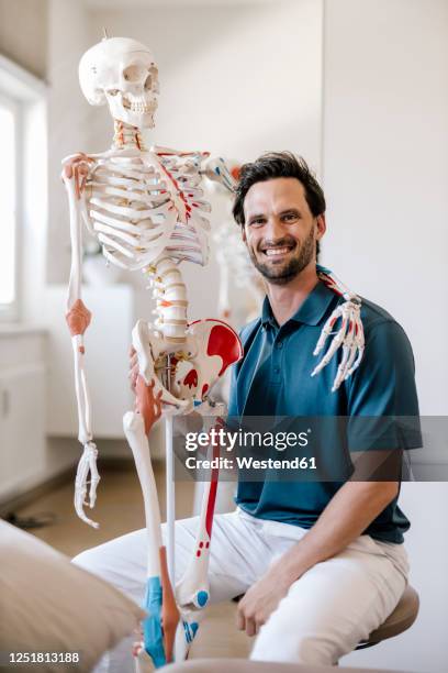 physiotherapist sitting in practice with skeleton arm around his shoulder - funny skeleton stock pictures, royalty-free photos & images