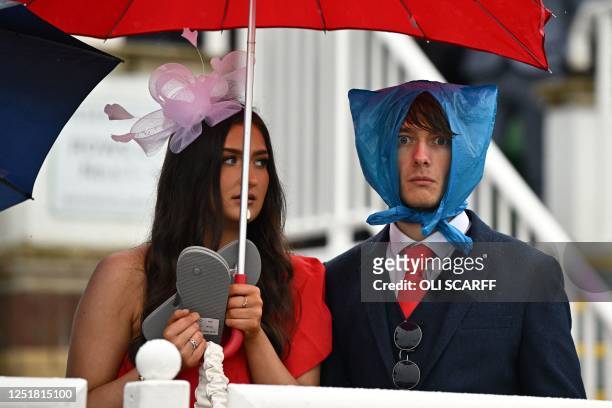 Racegoers shelter from the rain as they attend on the second day of the Grand National Festival horse race meeting at Aintree Racecourse in...