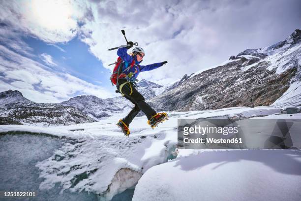 female mountaineer jumping over crevasse, glacier grossvendediger, tyrol, austria - crampon stock pictures, royalty-free photos & images