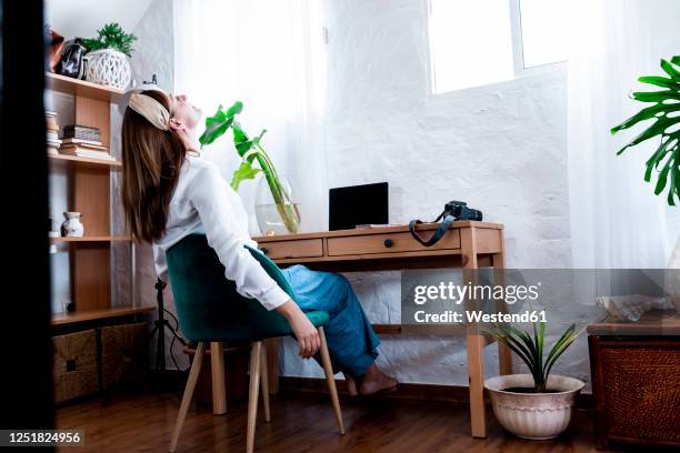 tired woman looking up while sitting on chair with head back at home - head on table stock-fotos und bilder