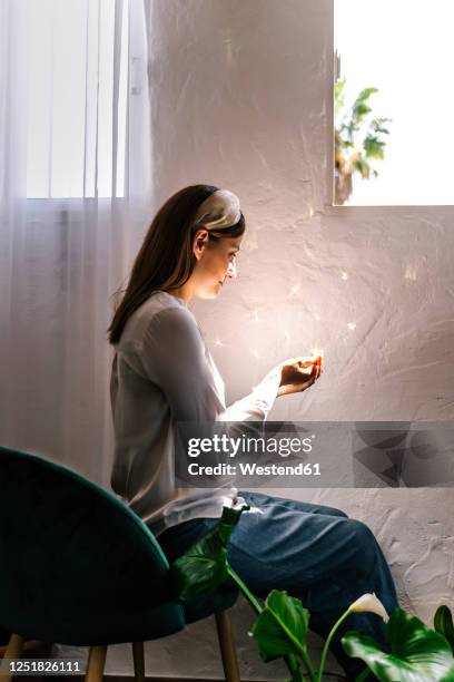 woman sitting on chair while looking at sunlight on cupped hands in bedroom - hands cupped stock pictures, royalty-free photos & images