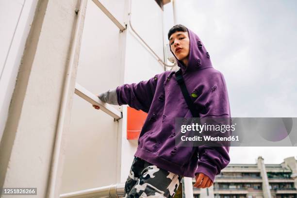 cool young man wearing hooded shirt standing on metallic ladder against sky - lilac fashin bildbanksfoton och bilder